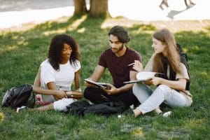 groupe-etudiants-internationaux-souriants-assis-herbe-ensemble-dans-parc-universite-filles-africaines-caucasiennes-garcon-indien-parlant-exterieur